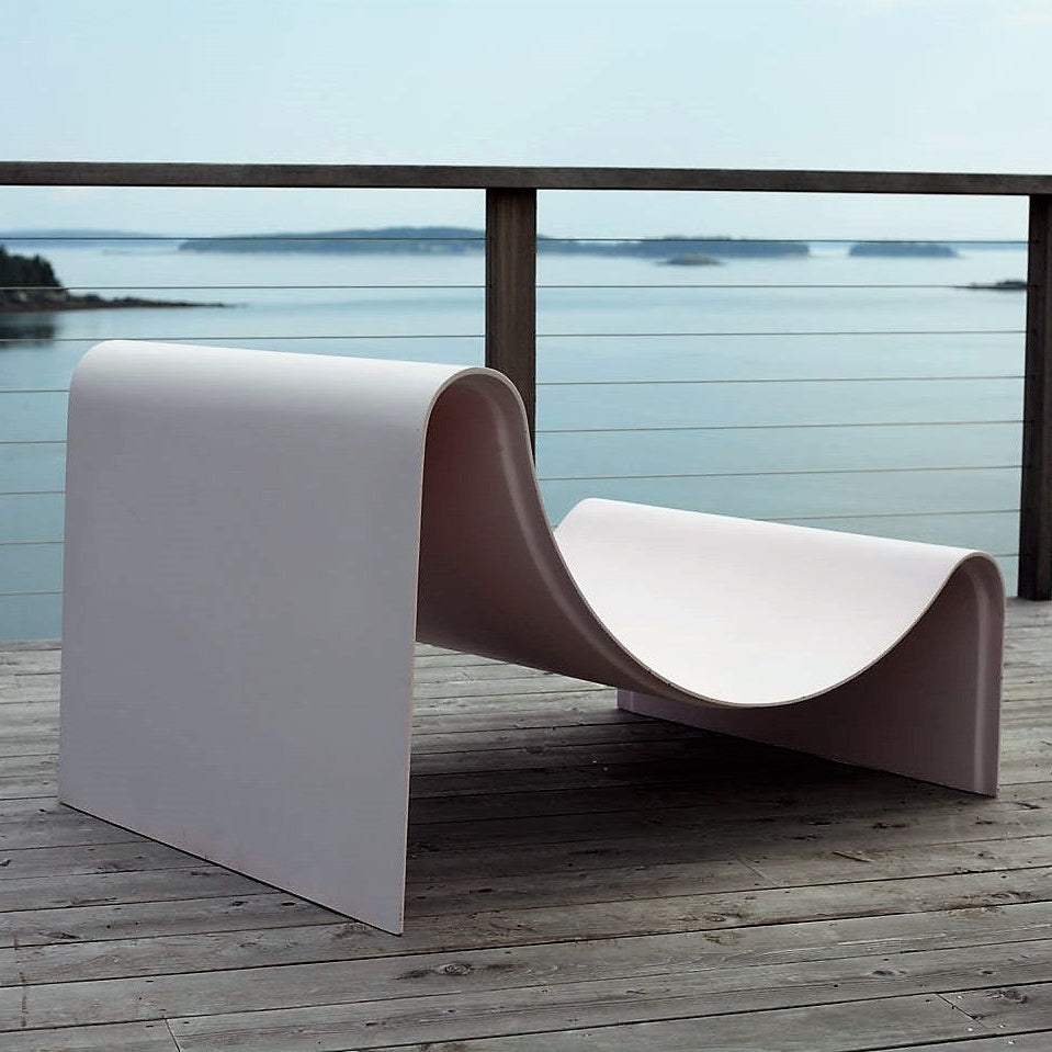Sleek minimal lounge chair on a wooden deck with a scenic water view.