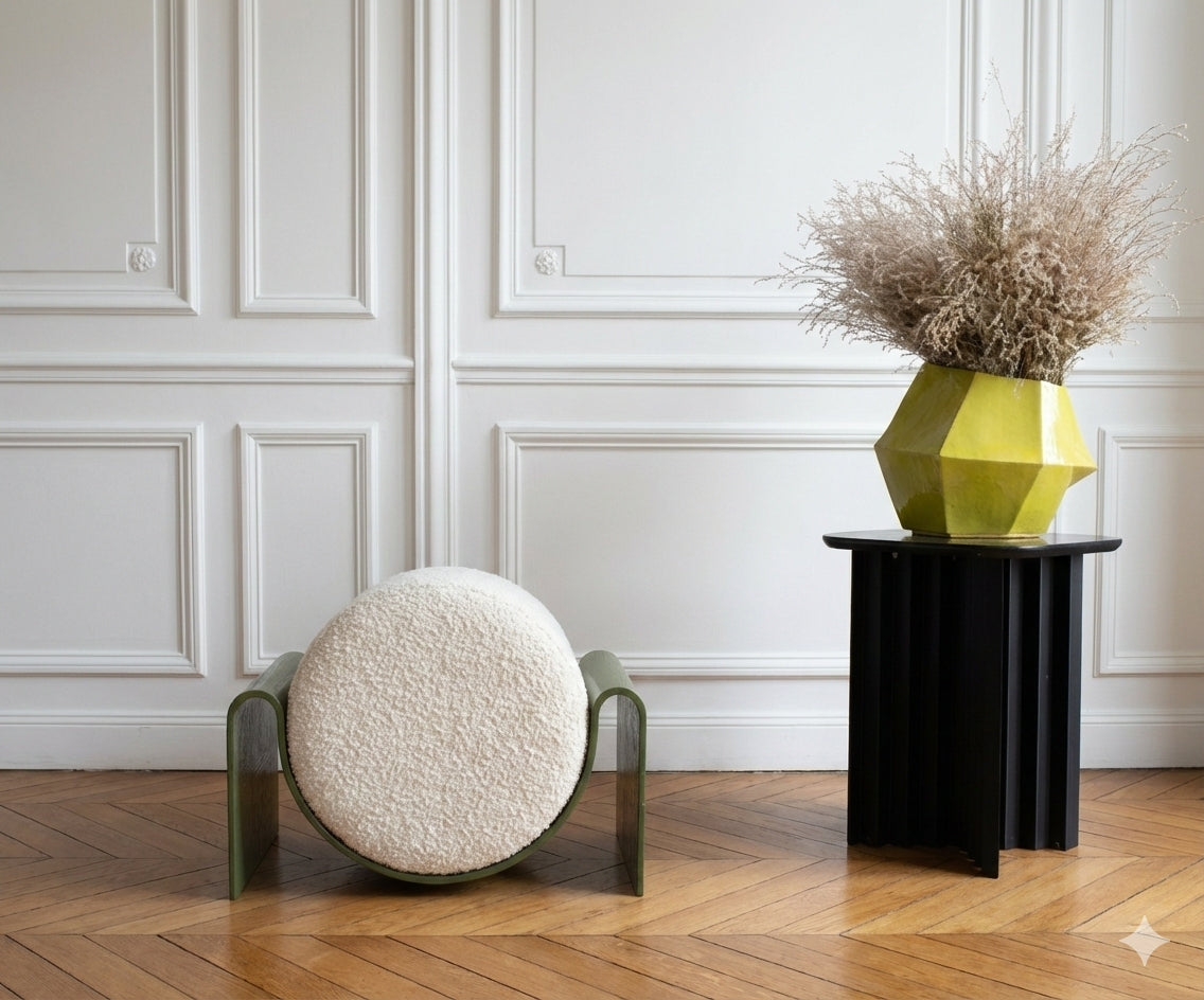 Round textured stool and black side table with a geometric yellow vase against a white paneled wall.