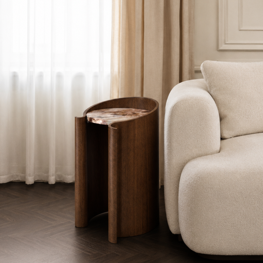 curved wood veneer side table in walnut with a marble top by a white couch in front of a window with drappy sheer curtains
